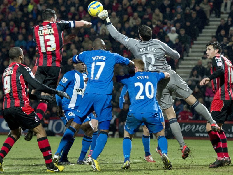 Wigan goalkeeper Mike Pollitt punches the ball clear in front of defender Tommy Elphick