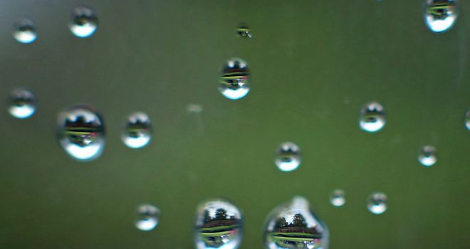 A view of the drenched course is reflected through raindrops on a window