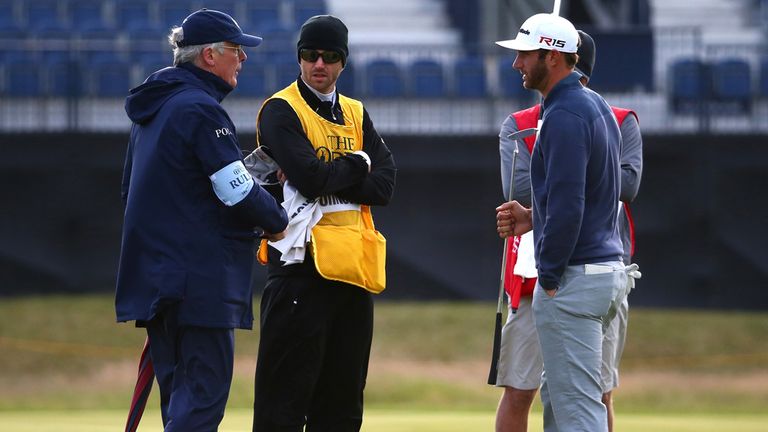 Johnson talks with a rules official on the 15th green as play is suspended due to high winds