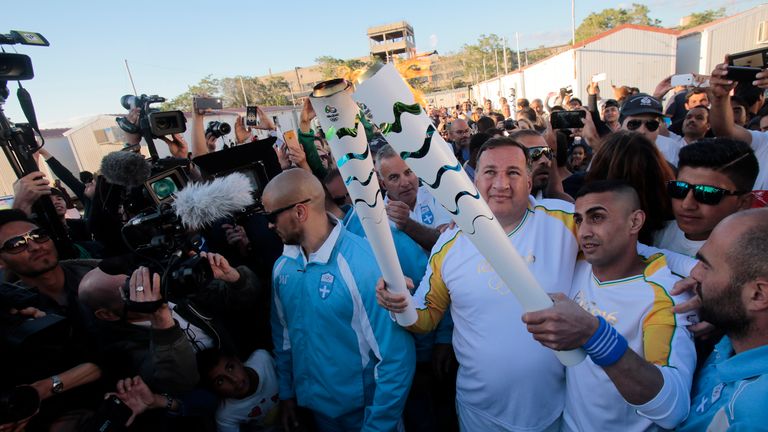 Ibrahim Al-Hussein (R) receives the Olympic flame from the head of Greece's Olympic Committee, Spyros Caprolas