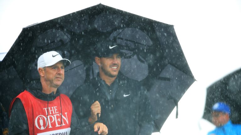 Koepka shelters from the rain with his caddie Ricky Elliott 