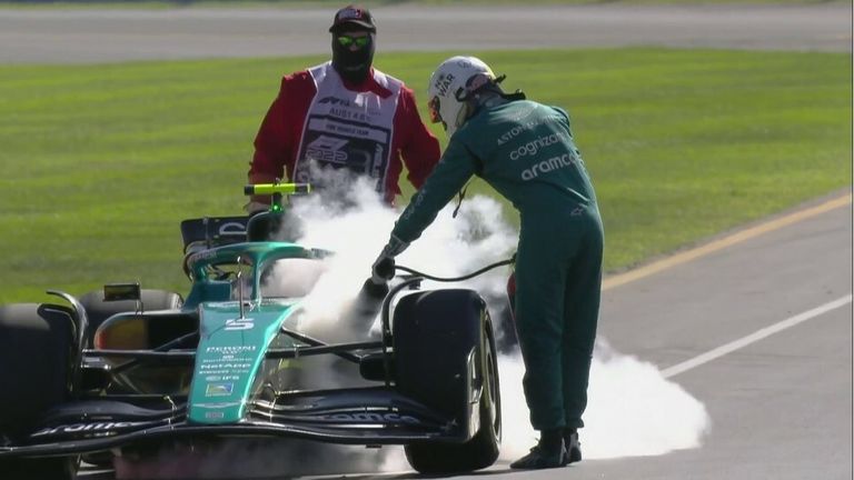 Sebastian Vettel runs to grab an extinguisher as his car's engine starts smoking. 